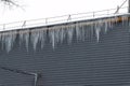 Many large ice icicles hanging from the edge of the roof and presenting a danger to people below