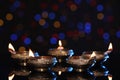 Many lit diyas on dark background with blurred lights, space for text. Diwali lamps