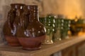 Many medieval earthenware jugs and cups in brown and green glazing standing on a wooden shelf near a stone wall Royalty Free Stock Photo