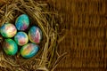 Many multi-colored Easter eggs lie in a nest of dry grass and twigs. Nest with eggs lie on the background of a table made of wicke Royalty Free Stock Photo