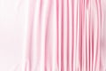 Many narrow vertical folds on a delicate pink fabric turn into a smooth background