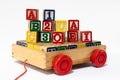 Many Numbers and letters colored wood blocks on a wooden cart with red wheels on white background.