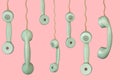 Many old telephone handsets from rotary landlines hanging from cords on pink background. Plastic grey removed receiver Royalty Free Stock Photo