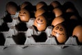 Many orange spotted brown chicken eggs in carton open box container in light with dark shadows. Three eggs with black drawn smile
