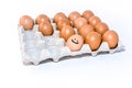 Many orange spotted brown chicken eggs in carton open box container on white background. One egg with drawn smile Royalty Free Stock Photo