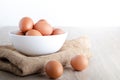 Many organic chicken eggs are placed in a white bowl on a wooden floor.