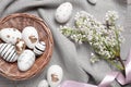 Many painted Easter eggs, branch with lilac flowers and ribbon on grey wooden table, flat lay Royalty Free Stock Photo