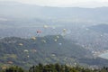 Many paragliders on bright colored parachutes fly in a misty mountain valley above the city aerial view