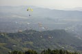 Many paragliders on bright colored parachutes fly over the city in a foggy mountain valley aerial view