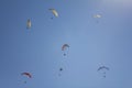 Many paragliders on colored parachutes fly against the background of clean blue sky and the sun