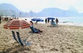 Many parasols and beach chairs and lot of people enjoy morning sunlight with the view of Rio de Janeiro of Brazil in backdrop