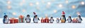 Many penguins with present boxes on blurred blue snowy background with copy space.