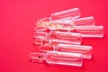 Many pharmaceutical transparent vials with medicine lie on red background. Concept photo of cycle of injection patient treatment,