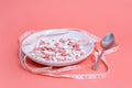 Many pink and white pills and capsules in white plate, spoon and measuring tape on pink background. Diet and weight loss Royalty Free Stock Photo