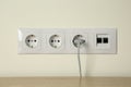 Many power sockets with plug and ethernet plate on white wall indoors