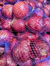 Many Red Onions in Purple Mesh Bags