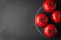 Many red and ripe raw tomatoes making a frame on a dark black and gray textured background. round stone serving plate, top view. Royalty Free Stock Photo