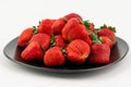 Many red ripe strawberries on a black plate isolated on white background Royalty Free Stock Photo