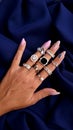 Many rings on a beautiful female hand on each finger on the background of dark blue fabric top view