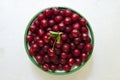 Many ripe red cherries in a white ceramic bowl with a green stripe on a light background. Harvesting concept. Royalty Free Stock Photo