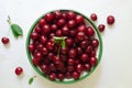 Many ripe red cherries in a white ceramic bowl with a green stripe on a light background. Harvesting concept. Royalty Free Stock Photo