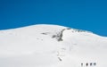 Many rope teams ascending a steep snow covered mountain slope.