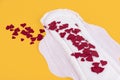 Many small red hearts, symbols of the menstrual cycle, on a feminine sanitary napkin. Feminine hygiene products during the