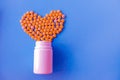 many small yellow pills spilled out of a white jar on a blue background in the shape of a heart Royalty Free Stock Photo