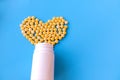 Many small yellow pills spilled out of a white jar on a blue background in the shape of a heart Royalty Free Stock Photo