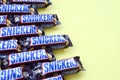 Many Snickers chocolate bars lies on pastel yellow paper. Snickers bars are produced by Mars Incorporated. Snickers was created by