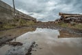 Many softwood logs lie along the road in mud and puddles on a cloudy fall afternoon at an old abandoned sawmill Royalty Free Stock Photo