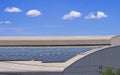 Many solar panels on top of curved steel roof of industrial building against cloud on blue sky Royalty Free Stock Photo