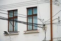 Many tangled electrical wires next to the window and wall of an old house. Problems of ill-conceived electrical wiring