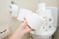 Many toilet paper rolls at home of hoarder, buying too much of hygienic means during pandemia, a hand holding a roll of