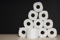 Many toilet paper rolls stacked in pyramid shape. Soft hygienic paper. Wooden table on black background Royalty Free Stock Photo