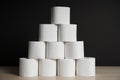 Many toilet paper rolls stacked in pyramid shape. Soft hygienic paper. Wooden table on black background Royalty Free Stock Photo