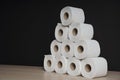 Many toilet paper rolls stacked in pyramid shape. Soft hygienic paper. Wooden table on black background Royalty Free Stock Photo