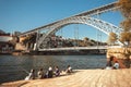 Many tourists sitting on riverside and making pictures of the iron bridge and city over river Douro