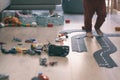 Many toy cars mess and road on a hardwood indoor floor playground with baby legs