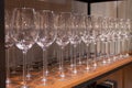 Many transparent crystal wine glasses stand in row on the brown wooden shelves of the rack. Side view. The concept of tasting
