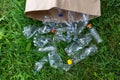 Many transparent empty water bottles are gathered in the paper bag on the green grass. Separate waste and recycle plastic bottles Royalty Free Stock Photo