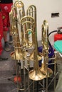 Many trombones stand around on their trombone stands in the aisle. Imperial College London big band rehearsal room. Brass