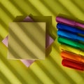 Many various rainbow colors pens with pink and yellow sticky note peper post it sheets lying on bright yellow background