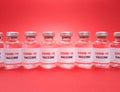 Many vials with covid 19 vaccine in a row on red background.