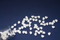Many of white candy heart-shaped pills spilled out of a transparent jar on a dark blue background. Royalty Free Stock Photo