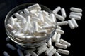 Many white medicine capsules in glass bowl and pills spilled around on black background. Pile of white tablets, medication Royalty Free Stock Photo