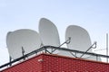 Many white parabolic satellite antena dishes on the roof of the house