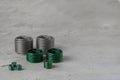 Many wire thread inserts of different size, green and grey color, free running on grey cement background. Stainless Steel.