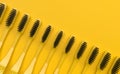 Many yellow toothbrushes with black bristles lie in a row on a yellow background. Creative conceptual illustration in bright