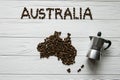 Map of the Australia made of roasted coffee beans laying on white wooden textured background with coffee maker Royalty Free Stock Photo